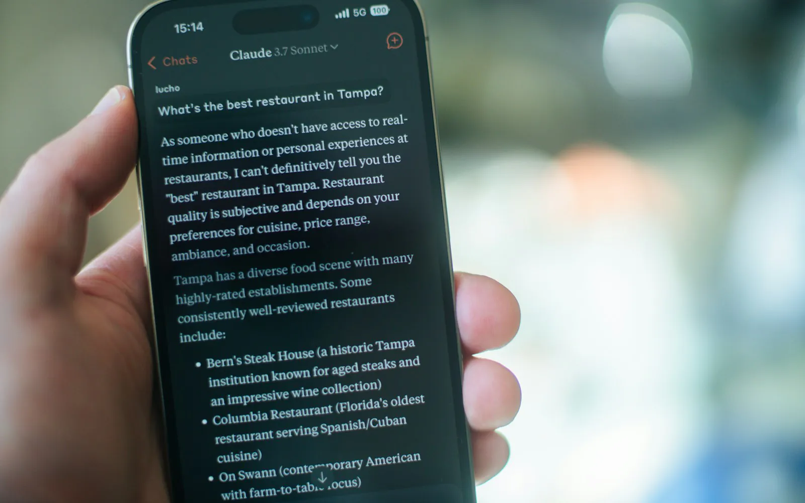 Hand holding a phone where an AI assistant answers “What’s the best restaurant in Tampa?” with a list of named restaurants