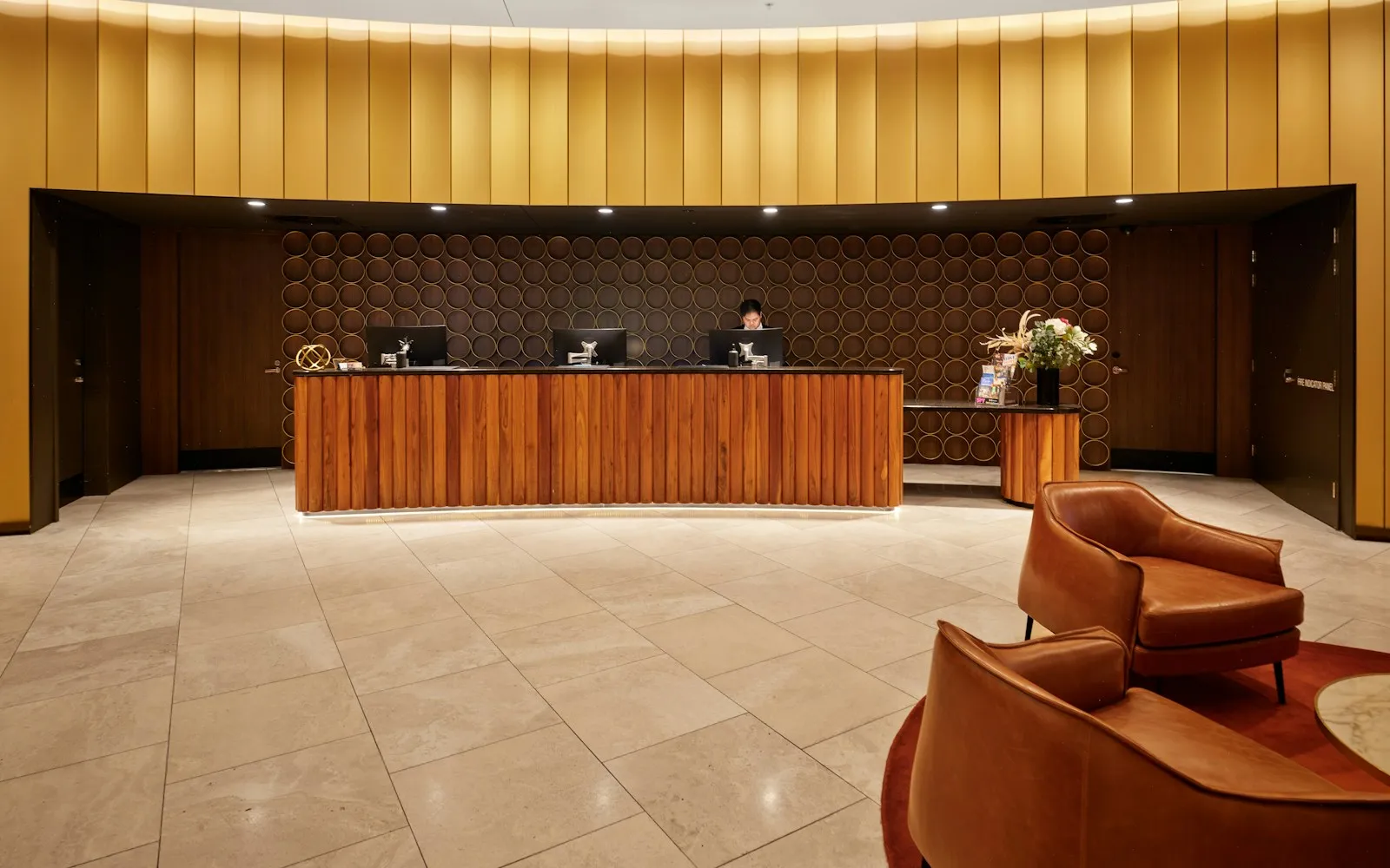 Hotel lobby with a curved wooden reception desk, gold panelled walls and leather armchairs