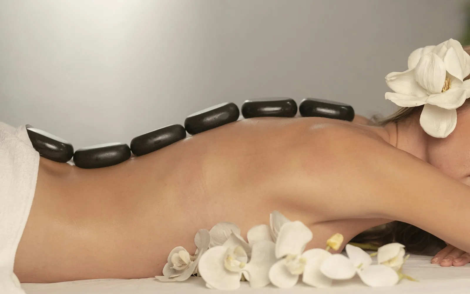 Person receiving a hot stone massage with white orchids on the treatment table