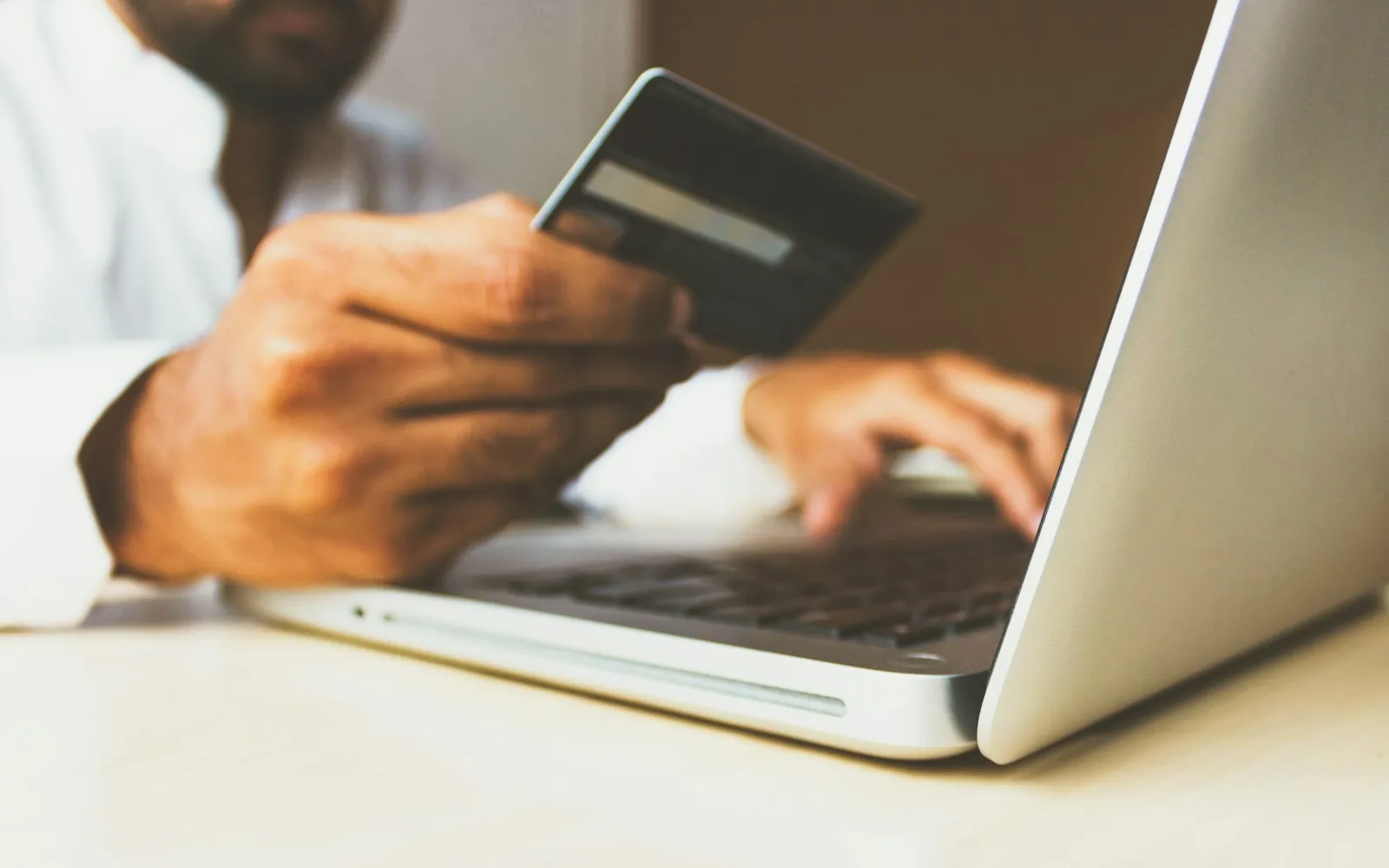 Man holding a credit card while typing on a laptop to shop online