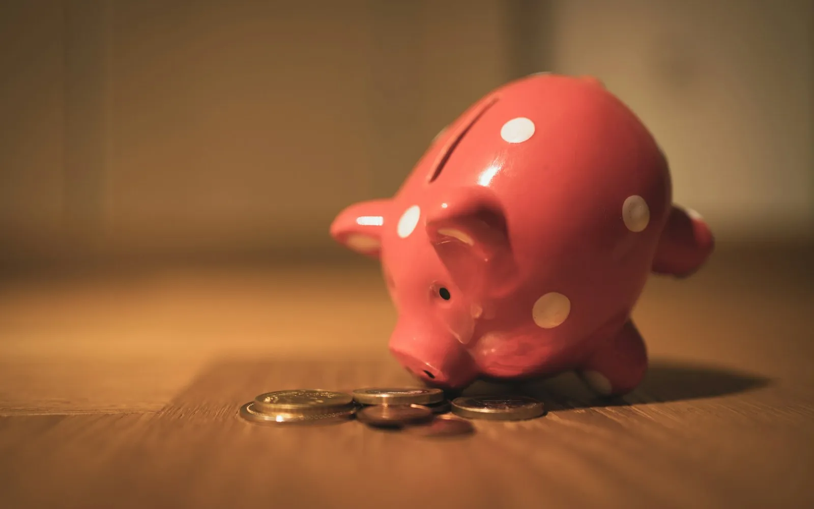 Red polka-dot piggy bank beside a small stack of coins on a wooden floor