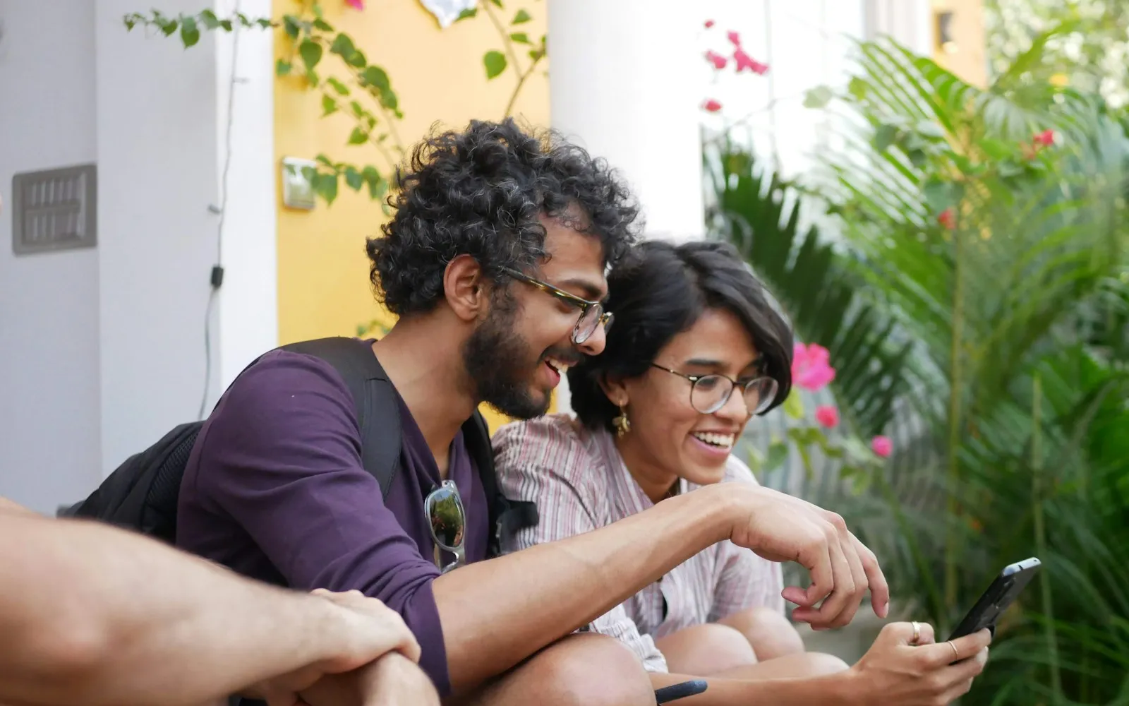 Two young friends laughing while looking at a smartphone outdoors
