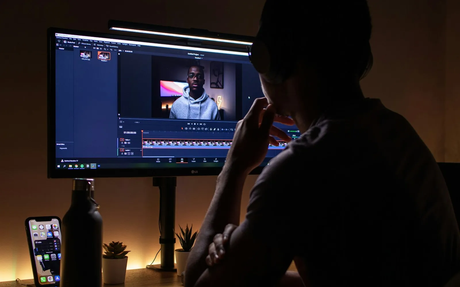 Person watching a video editing timeline on a monitor in a dark room lit by a screen bar