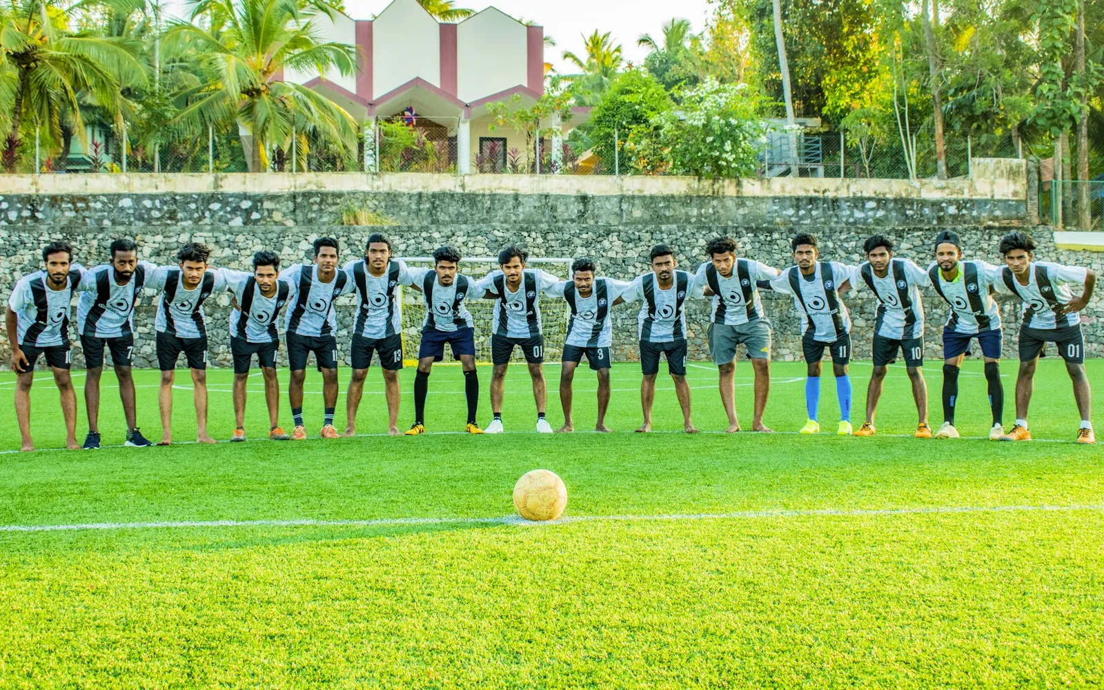 Football team in matching black and white jerseys lined up arm in arm on a pitch behind a ball