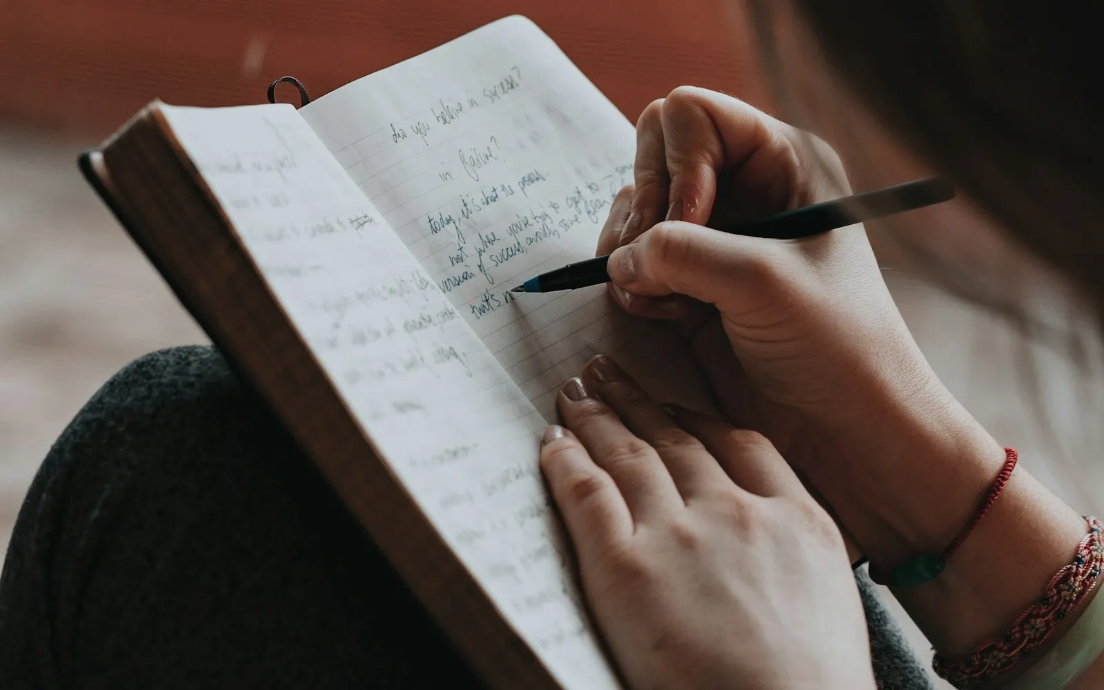 Hands writing notes in a lined notebook with a pen