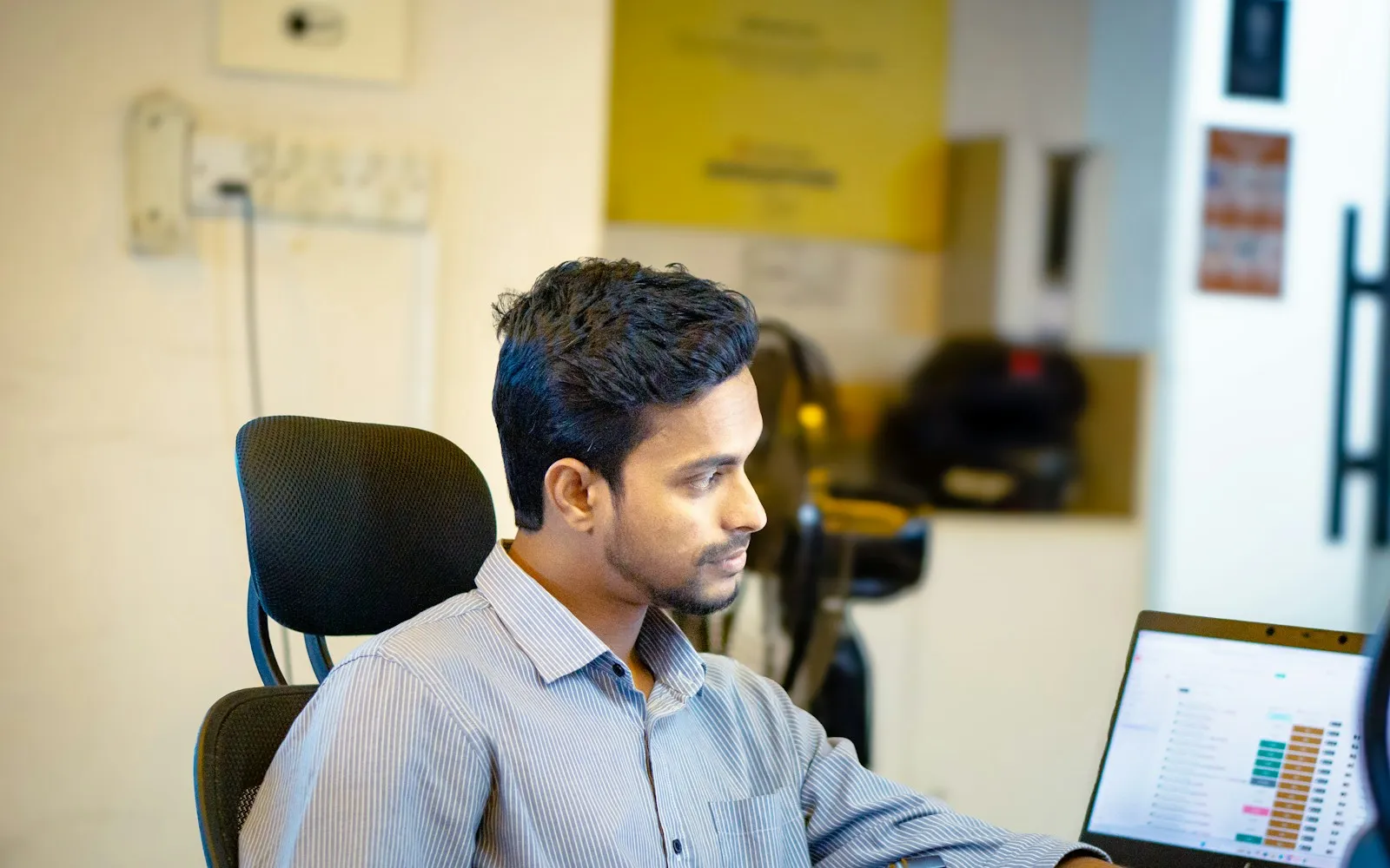 Man in a striped shirt looking at a spreadsheet on a laptop in an office