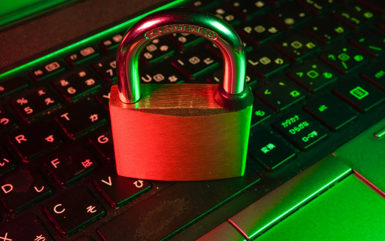 Brass padlock stamped Hardened resting on a laptop keyboard under red and green light
