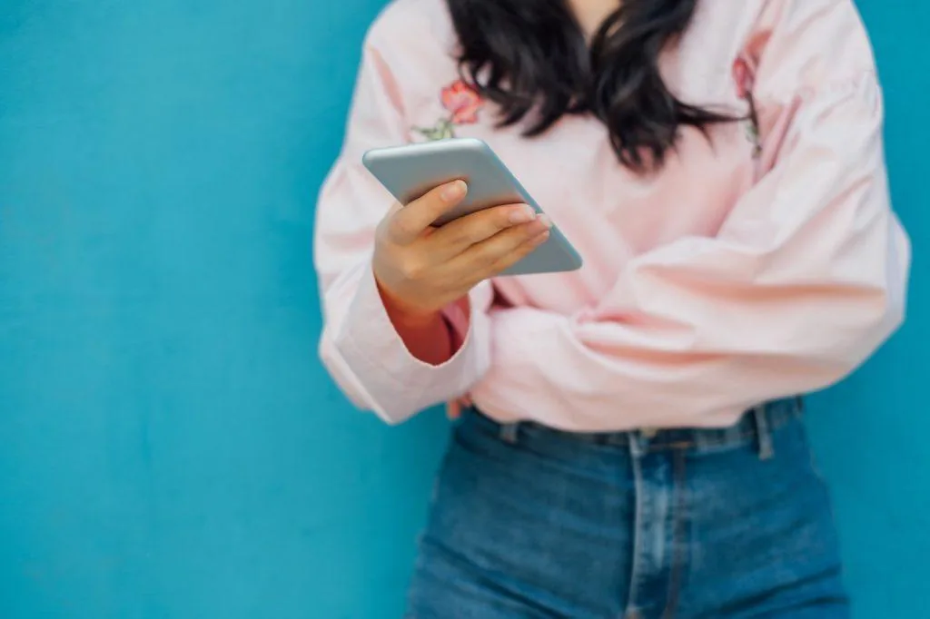 Woman in a pink shirt reading on her smartphone against a teal wall