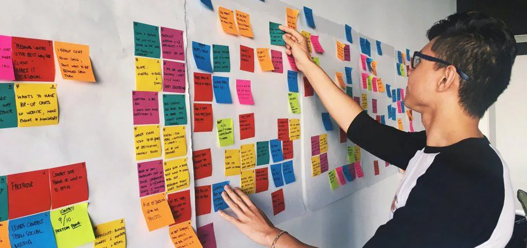 Designer arranging colorful sticky notes on a wall to group research findings during a design thinking session