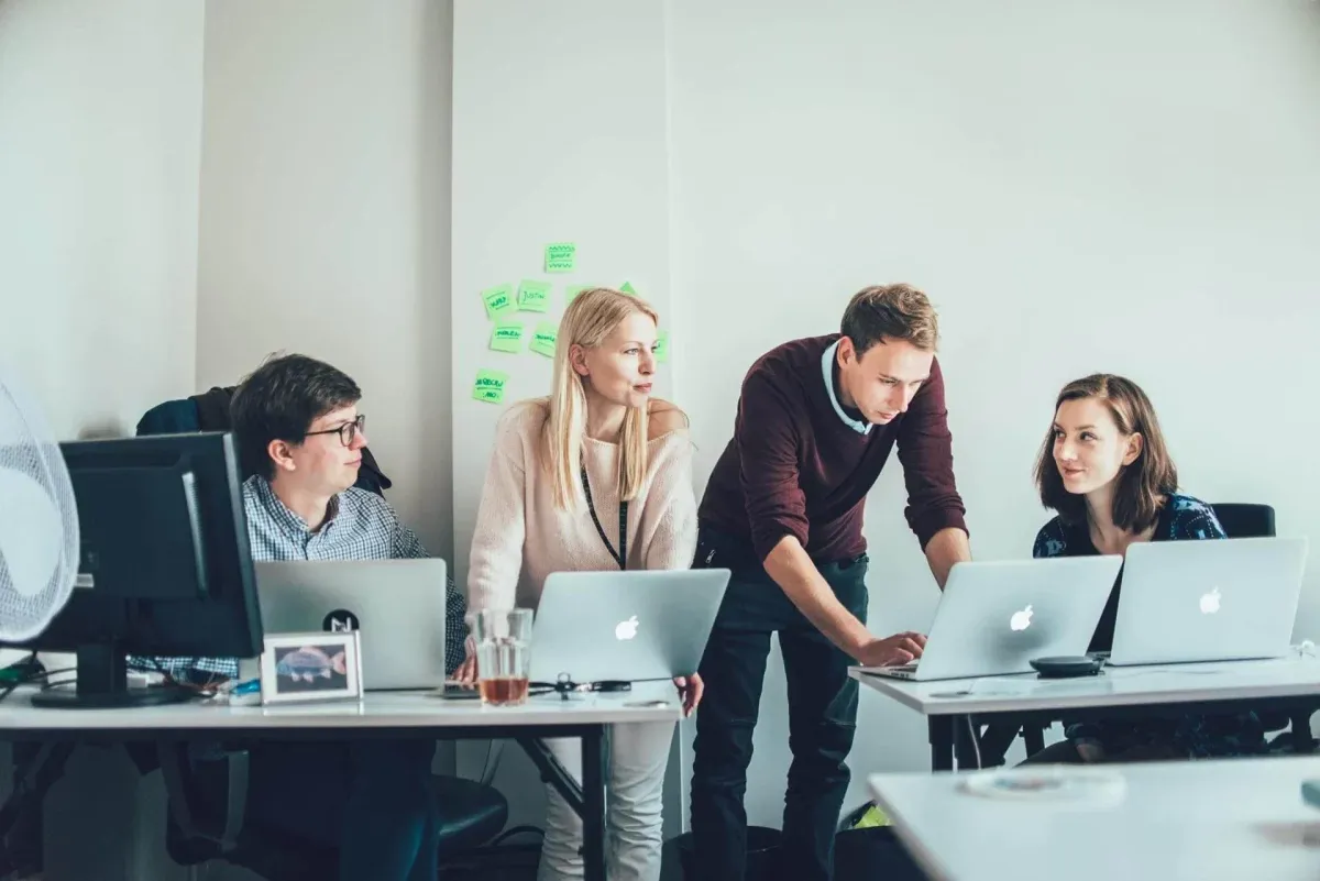Product team of four discussing work around laptops in a bright office with sticky notes on the wall
