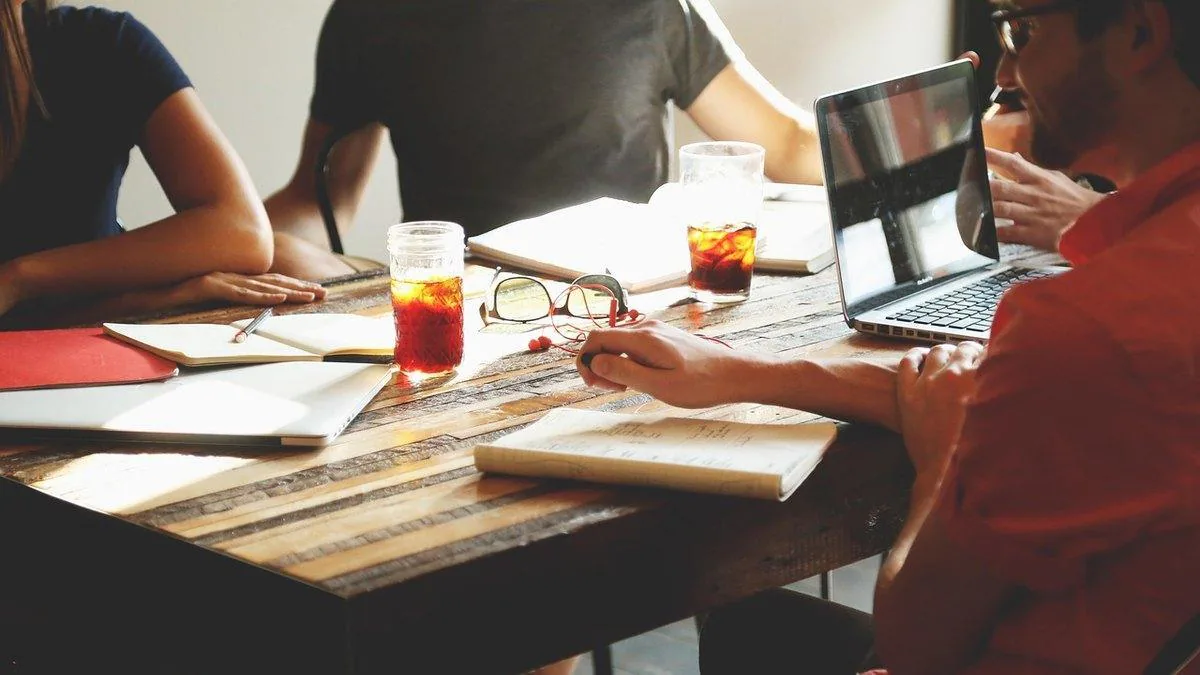 Colleagues around a wooden table with laptops, notebooks and iced drinks during a meeting