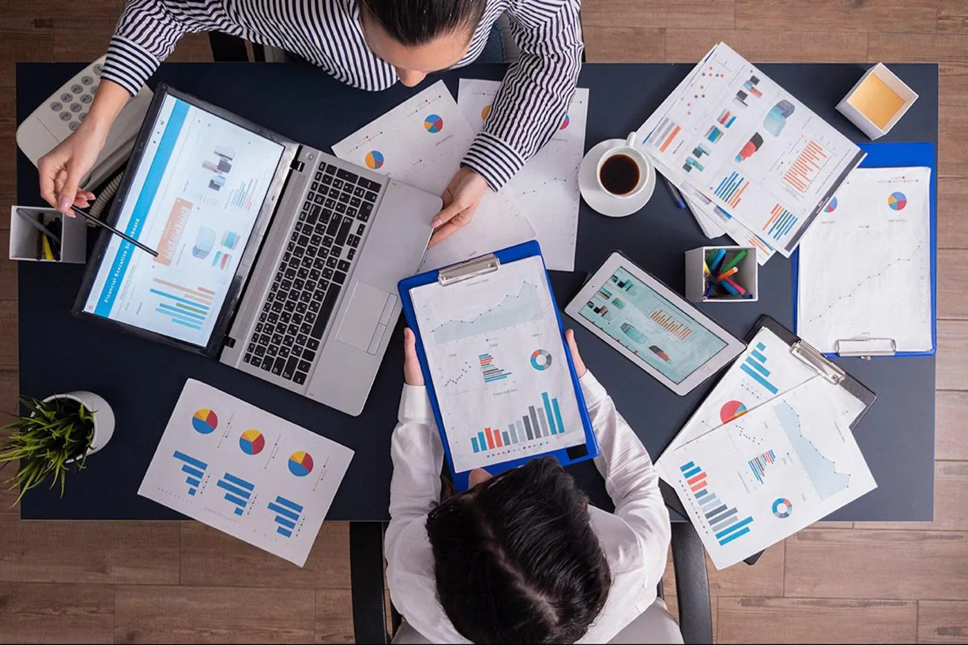 Overhead view of two colleagues reviewing charts and reports on a desk with a laptop and tablet