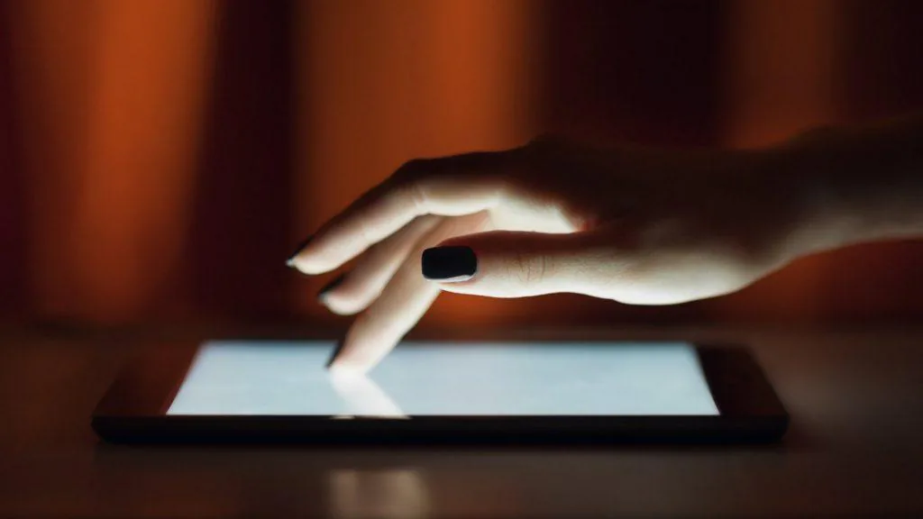 Hand touching a tablet screen in low light