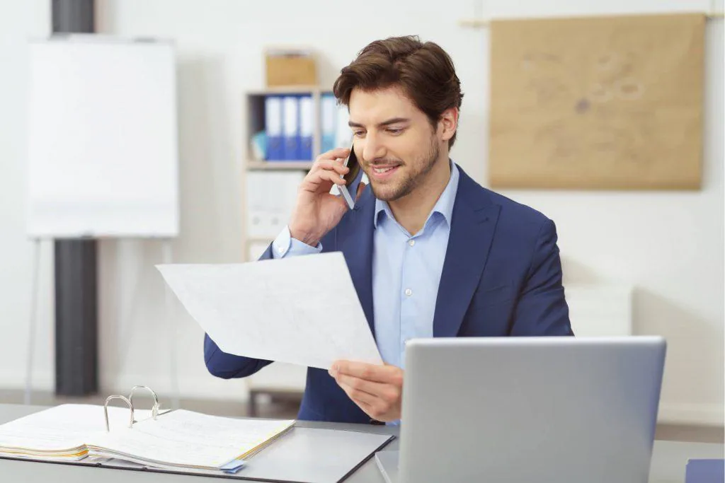 Businessman on a phone call reviewing printed figures at his desk