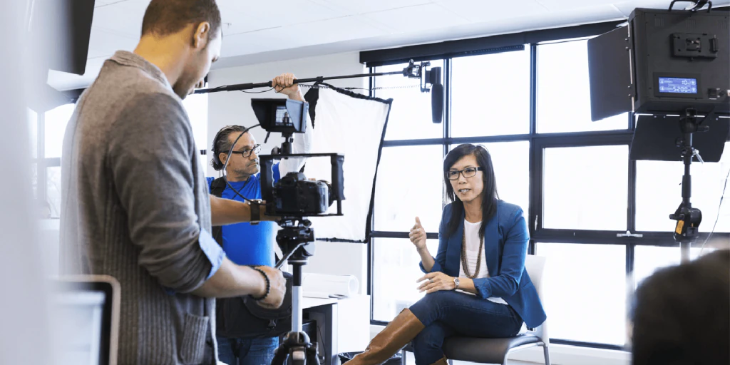 Video crew filming an interview with a woman seated in a bright studio