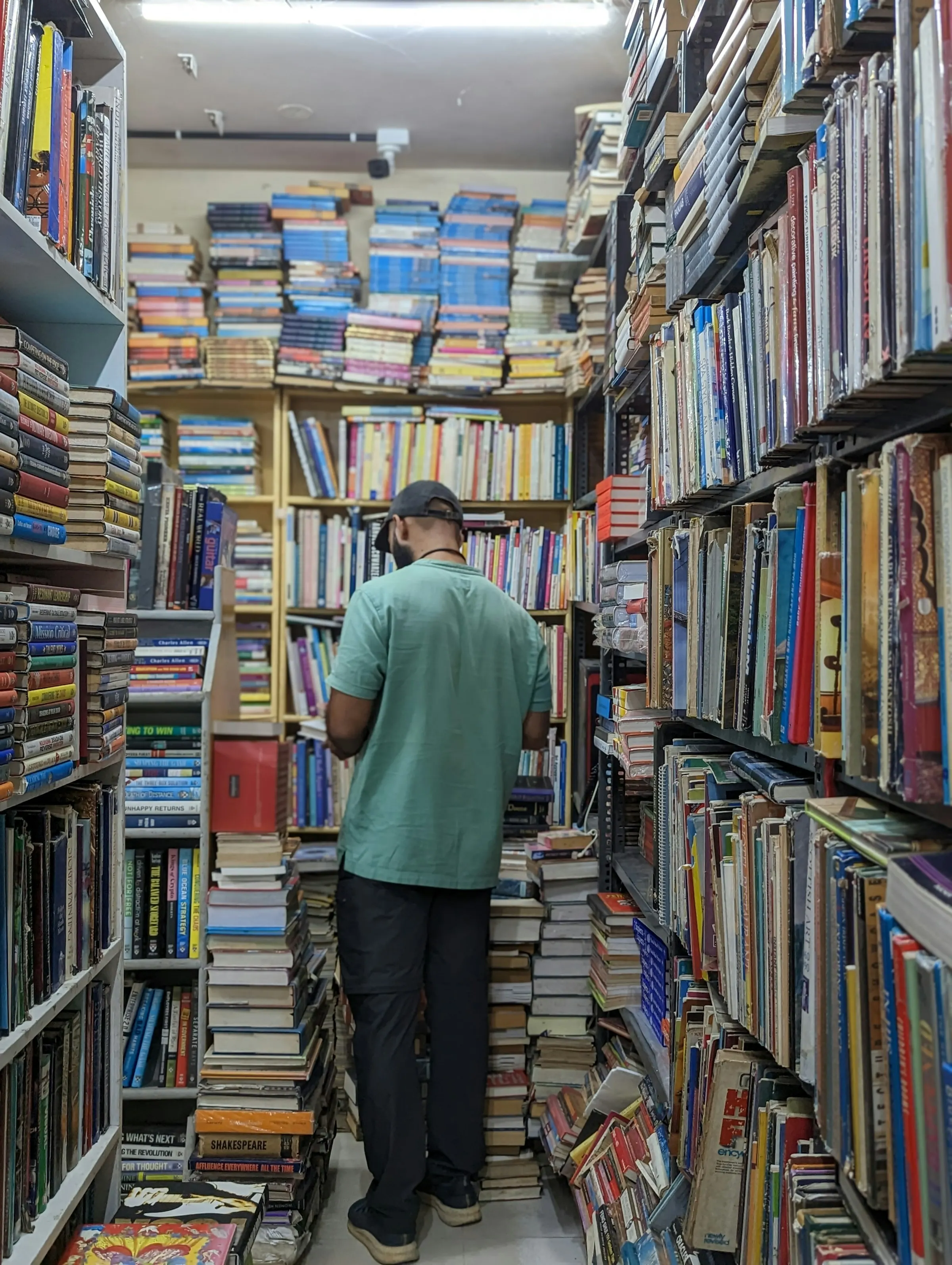 Man browsing tall, crowded shelves in a secondhand bookstore in Bengaluru