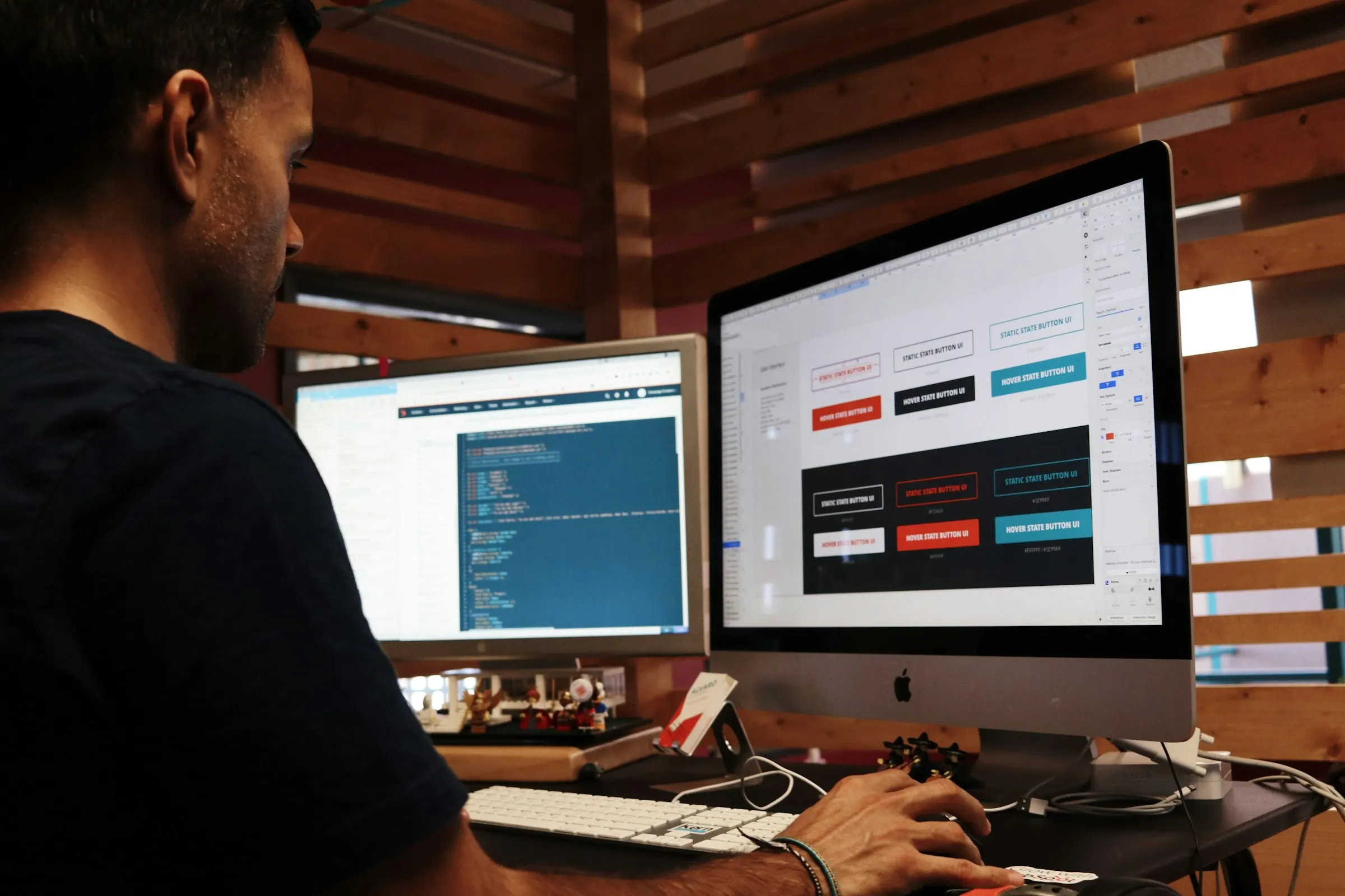 Designer working on button styles in a UI design tool on an iMac, with code open on a second monitor