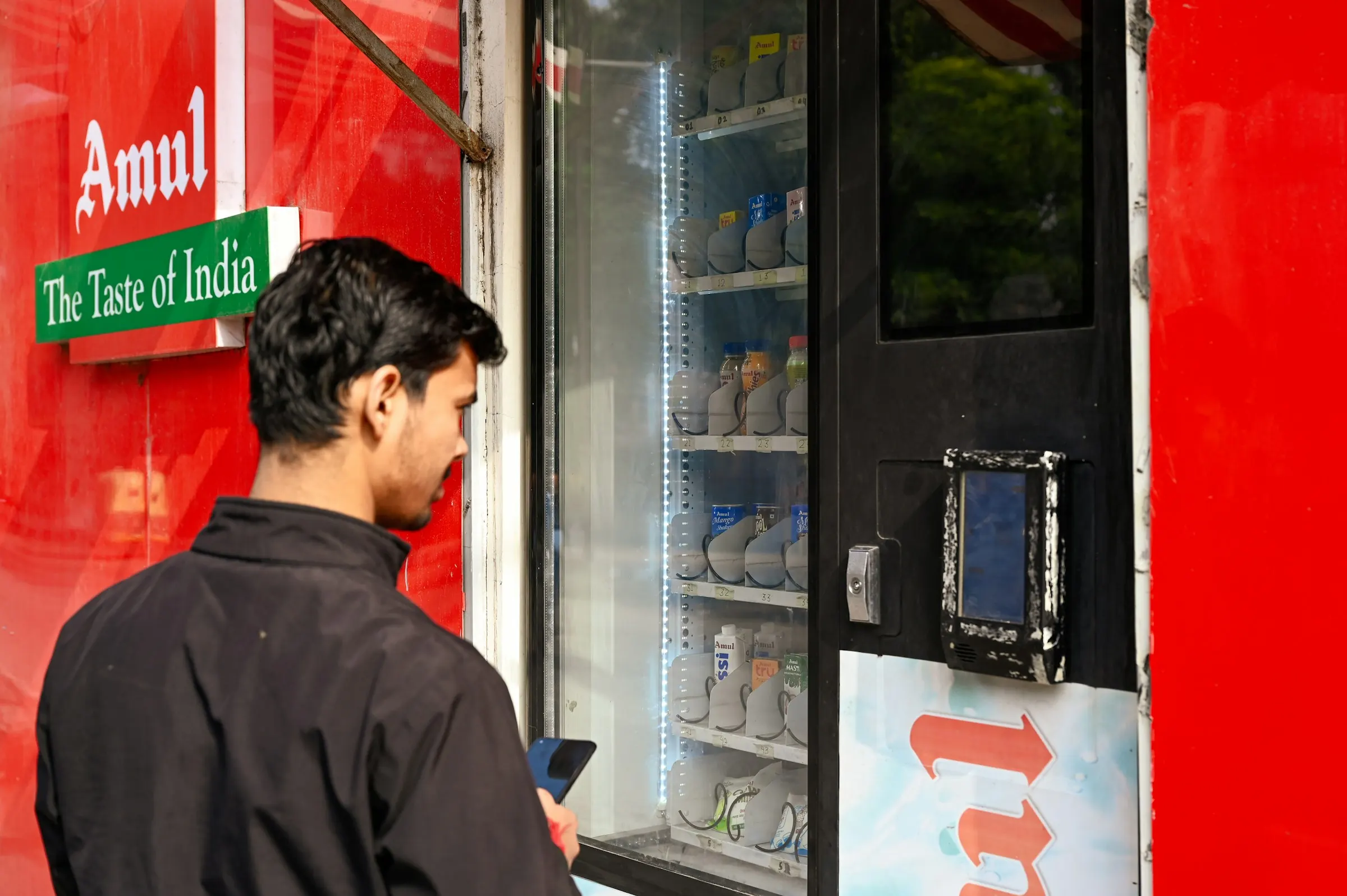 Man holding a smartphone to pay at an Amul vending machine in New Delhi