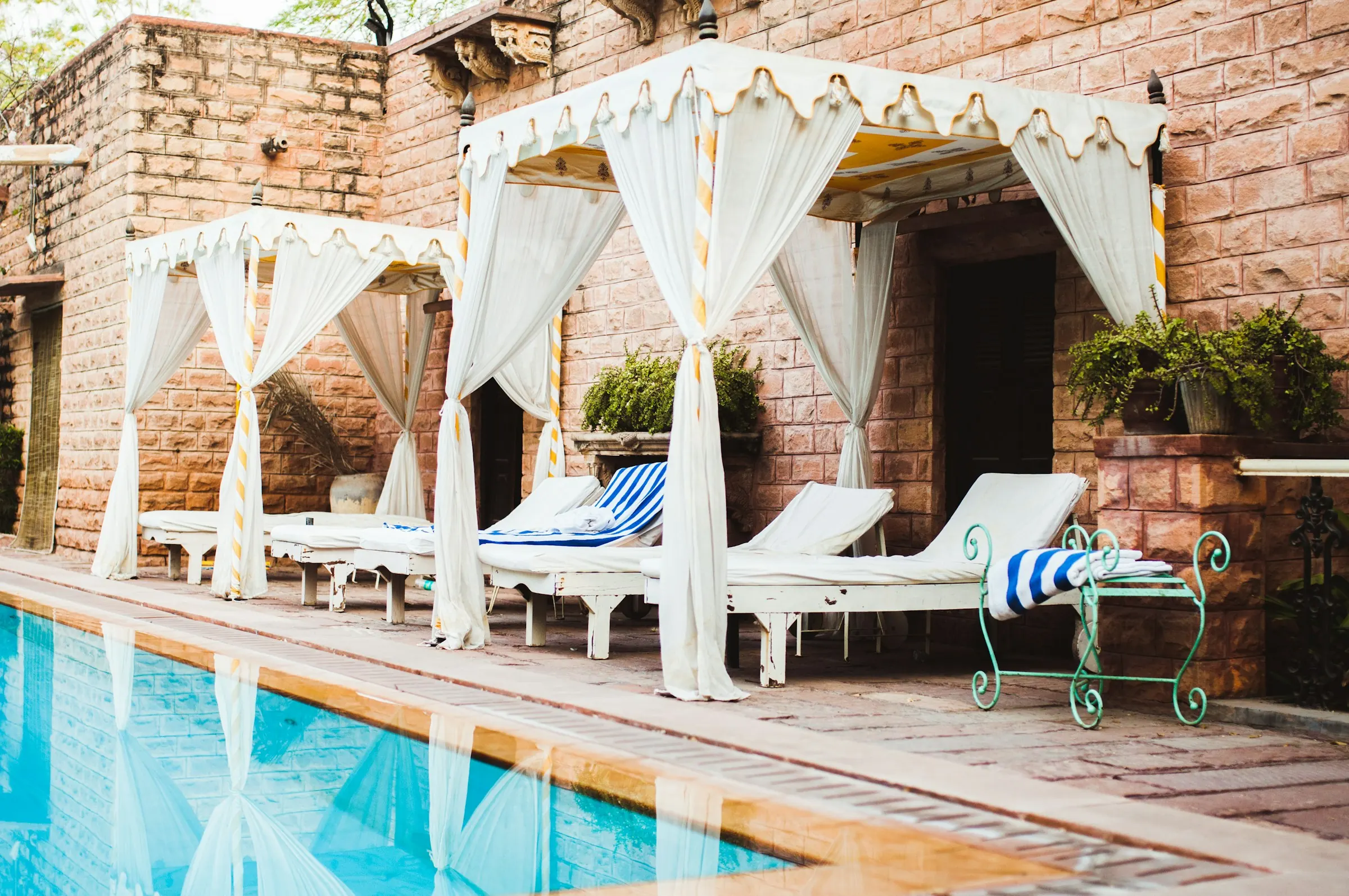 Canopied loungers beside a pool at a sandstone heritage hotel in Jodhpur