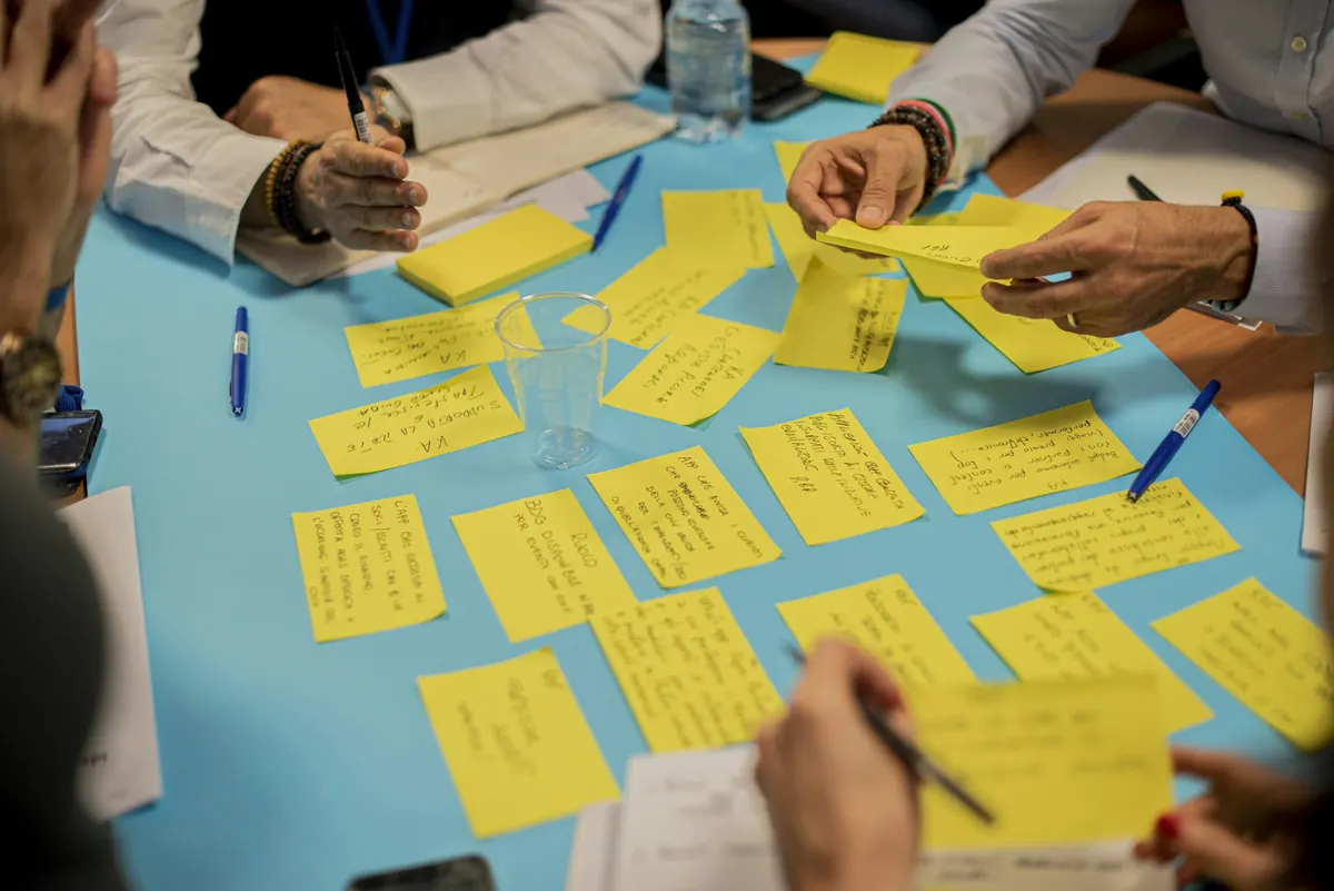 Hands sorting handwritten yellow sticky notes on a blue table during a planning workshop