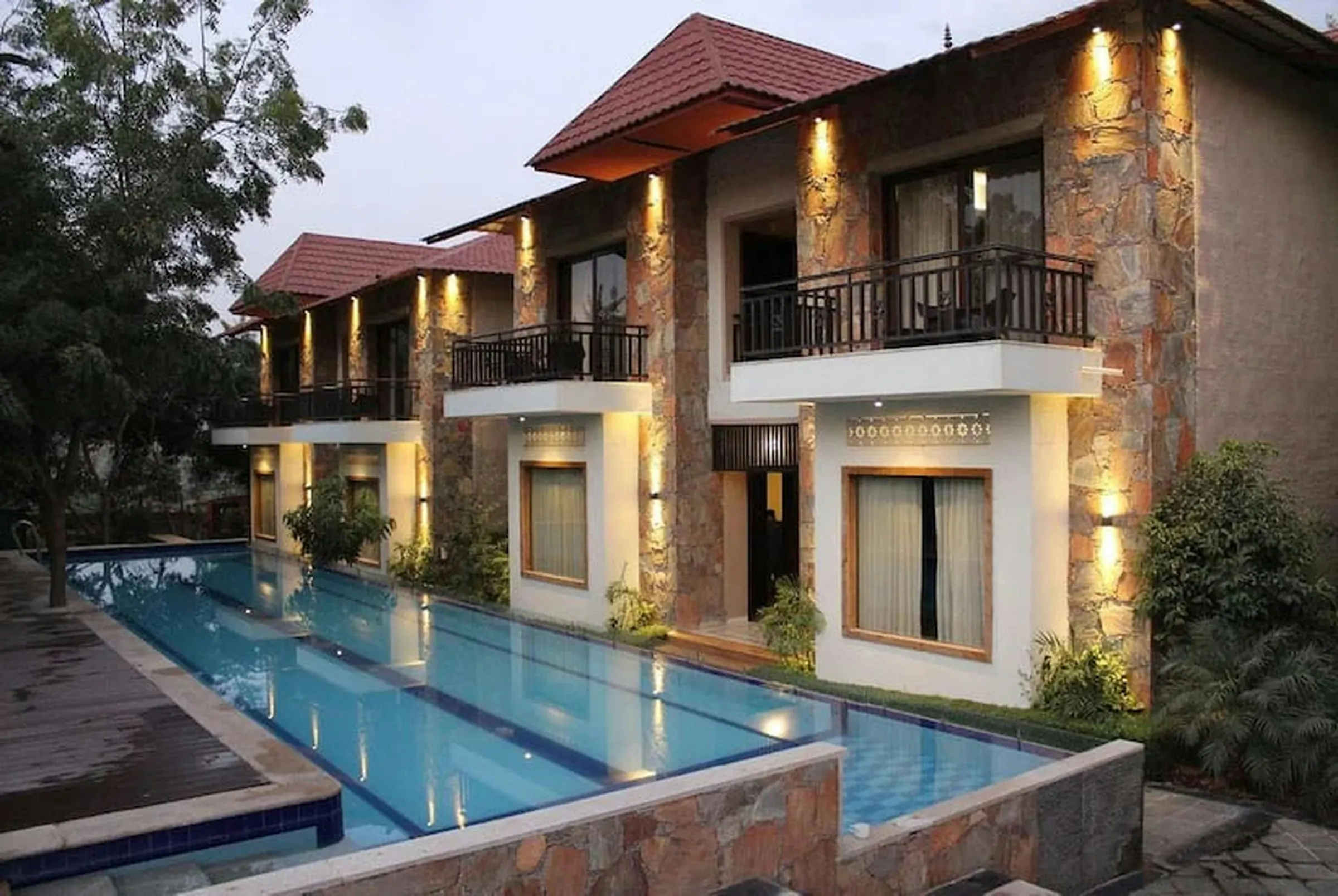 Two-storey stone villas with balconies above a lit pool in Udaipur at dusk