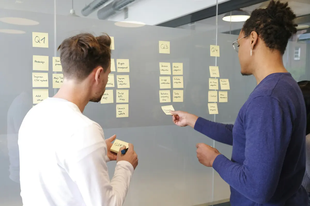 Two colleagues arranging handwritten sticky notes into a quarterly roadmap on a glass wall