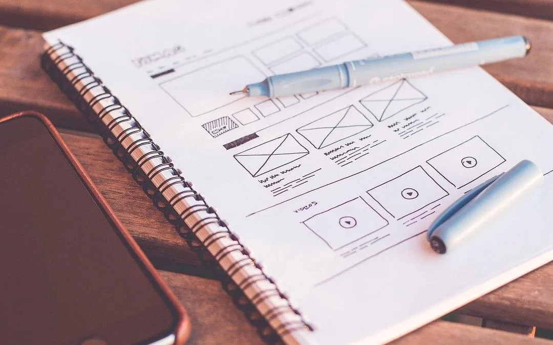 Designer sketching a landing page wireframe beside a laptop to improve website conversions